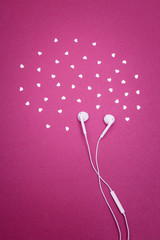 Earphones and hearts on bright magenta background