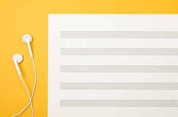 Fototapeta premium Earphones and blank music sheet on yellow background
