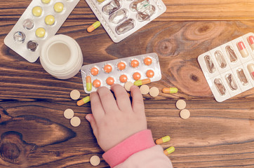 Children's hands with medicines on a wooden table. A small child left unattended plays dangerous...