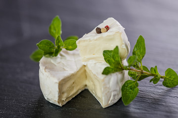 Brie type of cheese. Camembert cheese. Fresh Brie cheese and a slice on a black stone board leaves. Italian, French cheese.