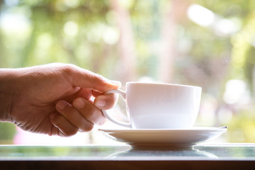 A man holding white coffee cup to drink when sitting near window