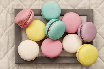 Fresh natural colorful macarons of different tastes in wooden frame on light napkin, top view, unusual abstract sweet art, gourmet gift