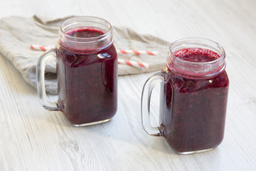 Glass jars with berry smoothie on white wooden surface, side view.
