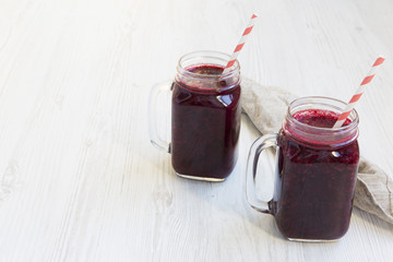 Glass jars with berry smoothie on white wooden surface, side view. Copy space.