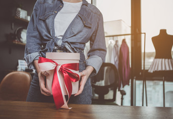 Close up female hands keeping attractive present with ribbon. She standing at table during job