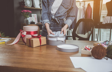 Close up female arms putting clothes in beautiful gift wraps while situating near desk during job