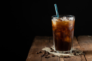 Ice coffee in a tall glass over and coffee beans on a old rustic wooden table. Cold summer drink on a dark background with copy space
