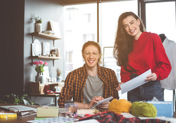 Portrait of beaming man and positive lady writing on papers while creating new collection of dresses. Fashion designer concept