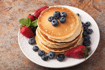 Close-up delicious pancakes, with fresh blueberries, strawberries and maple syrup on a rusty...