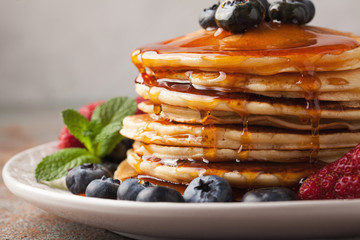 Close-up delicious pancakes, with fresh blueberries, strawberries and maple syrup on a light...