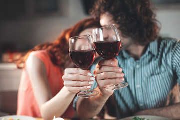 Happy loving couple is bonding to each other with fondness. Focus on glasses of red wine in their hands 