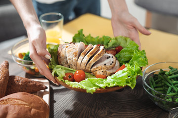 Close up of female hands holding plate with fresh meat and vegetables under the desk in kitchen 