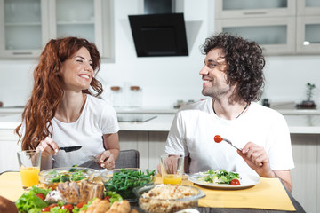 Obraz na płótnie Canvas Enjoy your meal, darling. Portrait of happy married couple is eating together in kitchen. They are looking at each other with love and smiling 