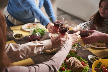 Close up of wine glasses holding by household members. They are sharing traditional wholesome dinner and spending time together