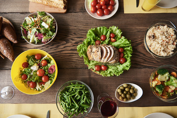 Top view of nutritious food cooked for tasty dinner. There are roast decorated with lettuce, veggie salads, bread, red cherry tomatoes and rice with spices