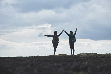 We are free. Happy two young women are standing on rock cliff and raising hands up. Final destination concept 