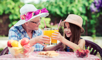 Grandparenting. Cute little girl drinking juice with her grandmother. Lifestyle, family life