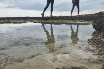 Fototapeta na wymiar Low angle close up of ocean water in natural pool at the stony coast. Two female tourists are going on background 