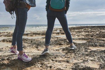 Close up of female legs standing on rocky shore. Women are traveling at the sea