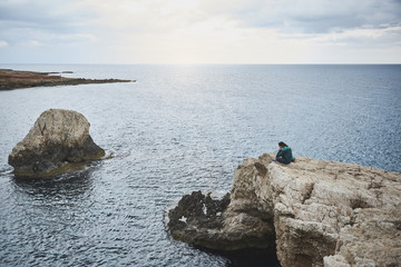 Nature calming down everyone. Peaceful girl is sitting on stone cliff and enjoying the sea view. Beautiful landscape concept 