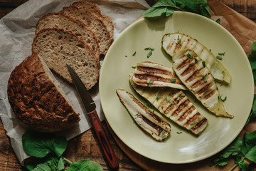 Grilled zucchini and freshly baked sliced bread on a wooden rustic table.  Flat lay.