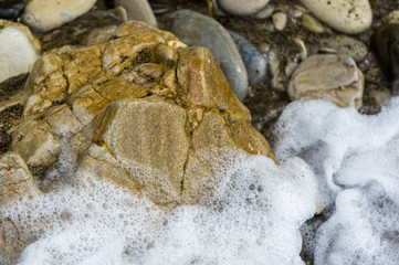 pebble stones on the sea beach, the rolling waves of the sea with foam