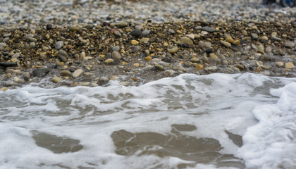 pebble stones on the sea beach, the rolling waves of the sea with foam