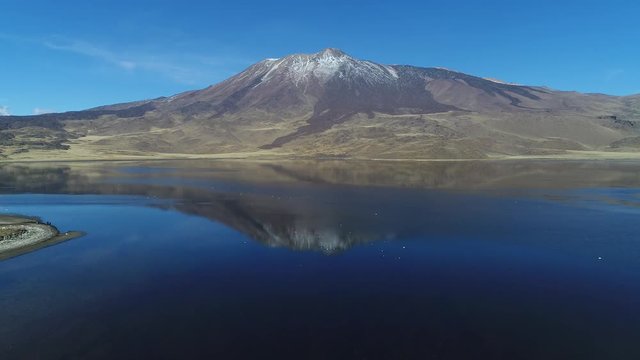Tromen volcano in national park, Patagonia. Aerial scene moving foward over the water. Mountain with bed of lava and snow. Tromen lagoon, refletion in front of the volcano. Wilde lonely landscape