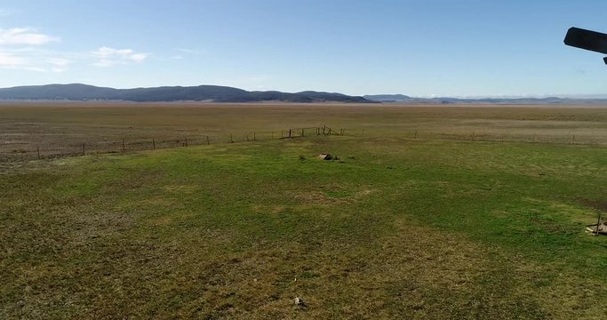 Dry land on the Lake George bed between distant hill ranges with windmill tower and cattle farm paddock in wide panorama.
