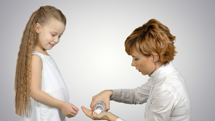 Mother giving her daughter medicine on white background