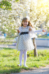 The girl listens to music from her mobile phone. Little girl in white dress listening to audio recordings in headphones in summer and park.