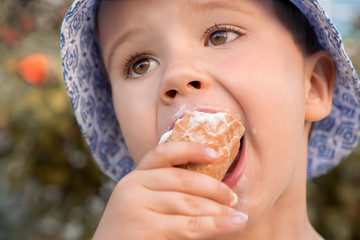 Naklejka premium Little child, boy eating ice-cream. Toddler boy eating dessert. Ice-cream in kid's hand. Child with ice-cream in cone, closeup. Portrait of little person with food. American human eating ice-cream