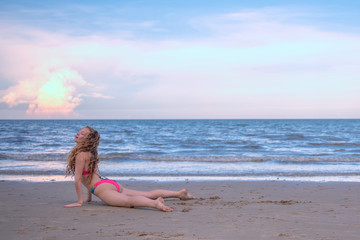 Fototapeta na wymiar Young healthy woman with blonde curly hair doing yoga on the beach, heathy and relaxing concept.