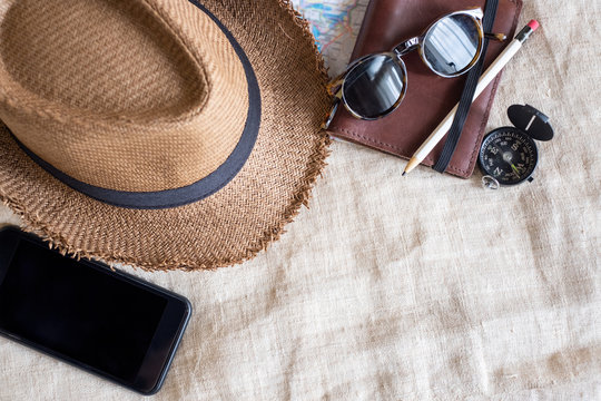 Top View Of Summer Brown Panama Straw Hat,mobile,sunglasses,notebook Map,compass On Linen Cloth.vacation Travel Concept.copy Space For Adding Text.