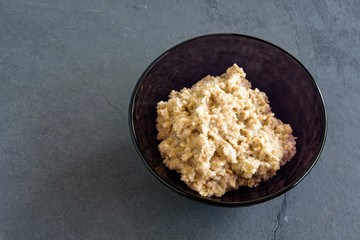 Fresh cooked oatmeal in a purple glass bowl on a slate background
