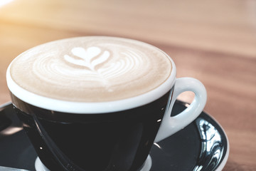 Cappuccino coffee in black cup on wooden table,ready for breakfast