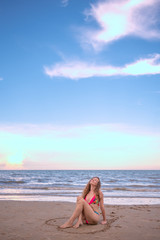 Happy young blond wavy hair woman sitting in heart shape that drawing on the beach, relaxing time concepts.