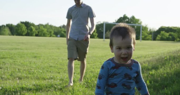 Toddler running towards camera with father behind him - slow motion