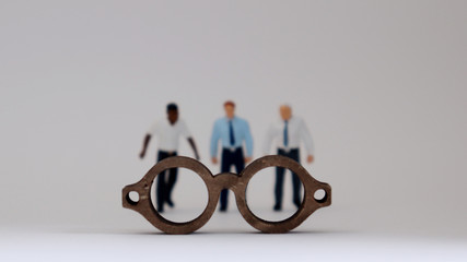 A social prejudice against race. Miniature people standing behind wooden miniature glasses.