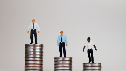 The concept of an economic income gap. Miniature people standing on pile of coins.