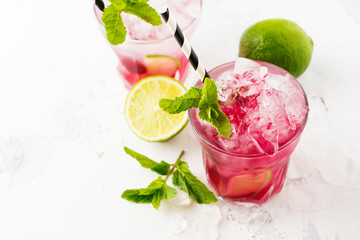 Red Summer cooling drink with ice, lime, raspberries and syrup on light background. Selective focus.