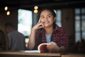 Young woman reading book sitting thinking indoor in urban cafe.