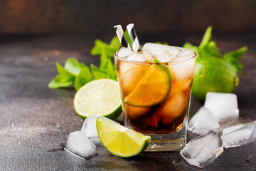 Fototapeta premium Summer cooling alcoholic beverage from cola, whiskey, lime and liqueur in glass on dark concrete old background.
