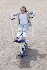 Obraz premium A young teenage girl in a gray sports suit, with long hair smiling and doing outdoor exercises on street exercisers.