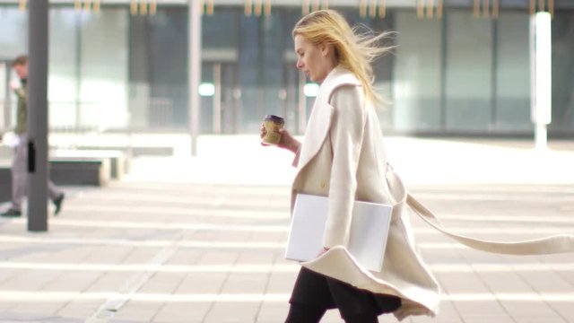 business woman with laptop and coffee walking down the street