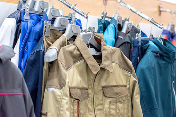 The upper work clothes of strong fabric of different colors with pockets hang on the hangers as a sample