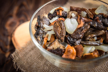 Golden fried forest mushrooms with onion in a bowl on wooden background with copy space.