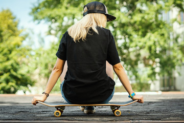 girl in a black T-shirt is sitting with her back on a skateboard and looks around