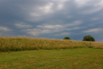 Ciemne, ciężkie, zachmurzone niebo nad płaskim krajobrazem, niedysoka skarpa porośnięta trawą, 