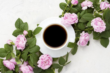 White cup with black coffee and pink roses on a light stone background. Flat lay, top view